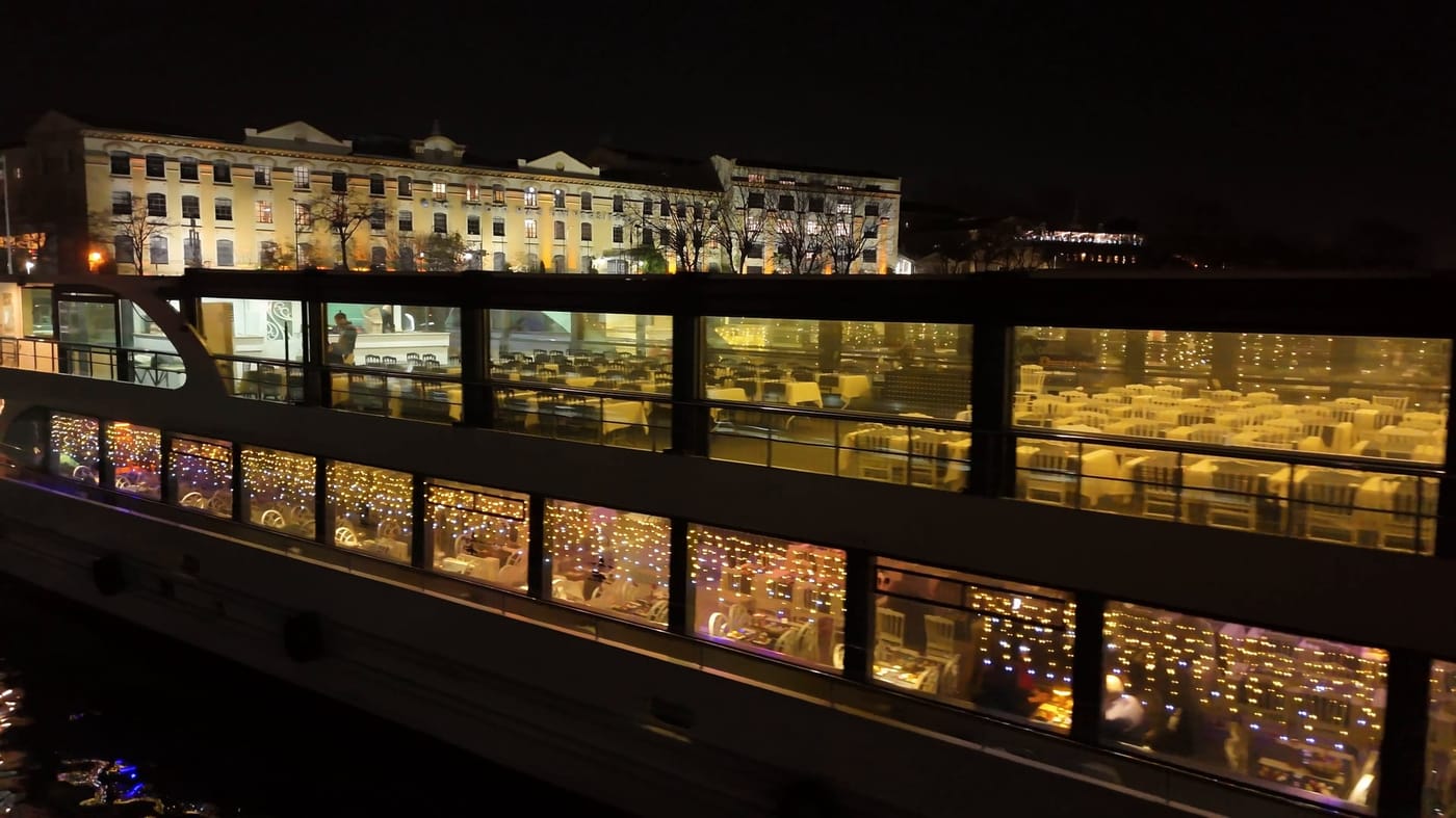 The boat lit up at night, tables visible through the salon windows