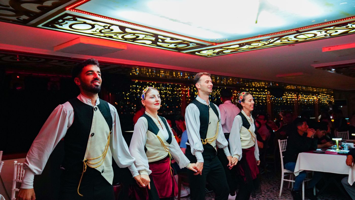 Dancers in embroidered waistcoats cross the salon