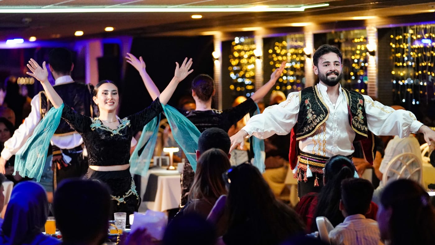 Dancers in embroidered waistcoats cross the salon