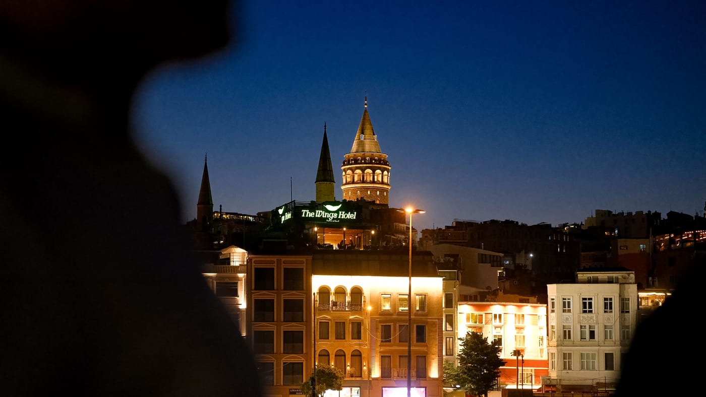 Galata Tower lit at dusk, a guest in silhouette in front